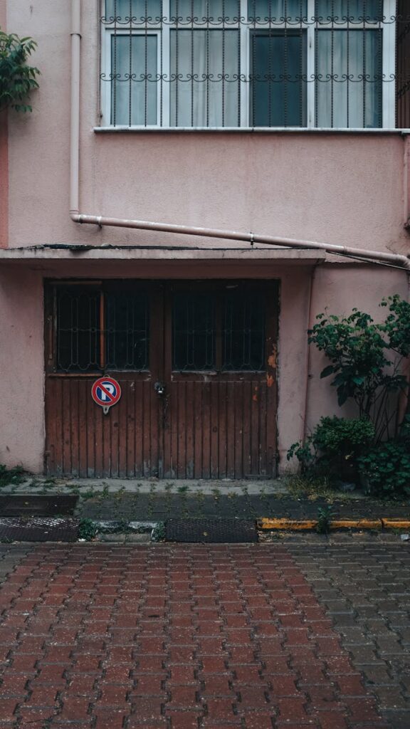 Weathered garage door in an urban setting with a no parking sign on wet pavement.